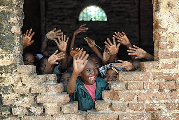 istockphoto-477437511-612×612 A group of african children inside of a destroyed school, wave hands and say hello.